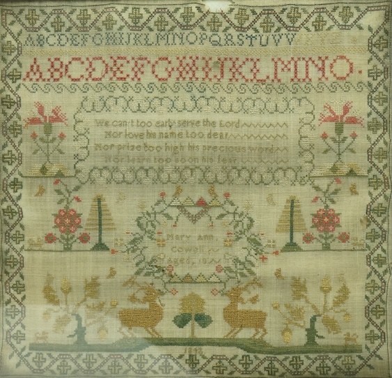 A 19th century flame figured mahogany framed cross stitch sampler dated 1842 by Mary Ann Cowell aged 10 years. Worked with the alphabet, verse and spot motifs of flowers, trees, dogs and deer, within an ornate border. 28